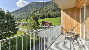 A balcony with a view of a green valley and mountains, a wooden exterior wall, and a table with chairs. - Studio in der Alpine Lodge Arlberg (Klösterle am Arlberg)