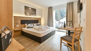 A modern hotel room with a large bed, a wooden headboard, a small desk with a chair, a television, and a window with curtains. - Studio in der Alpine Lodge Arlberg (Klösterle am Arlberg)
