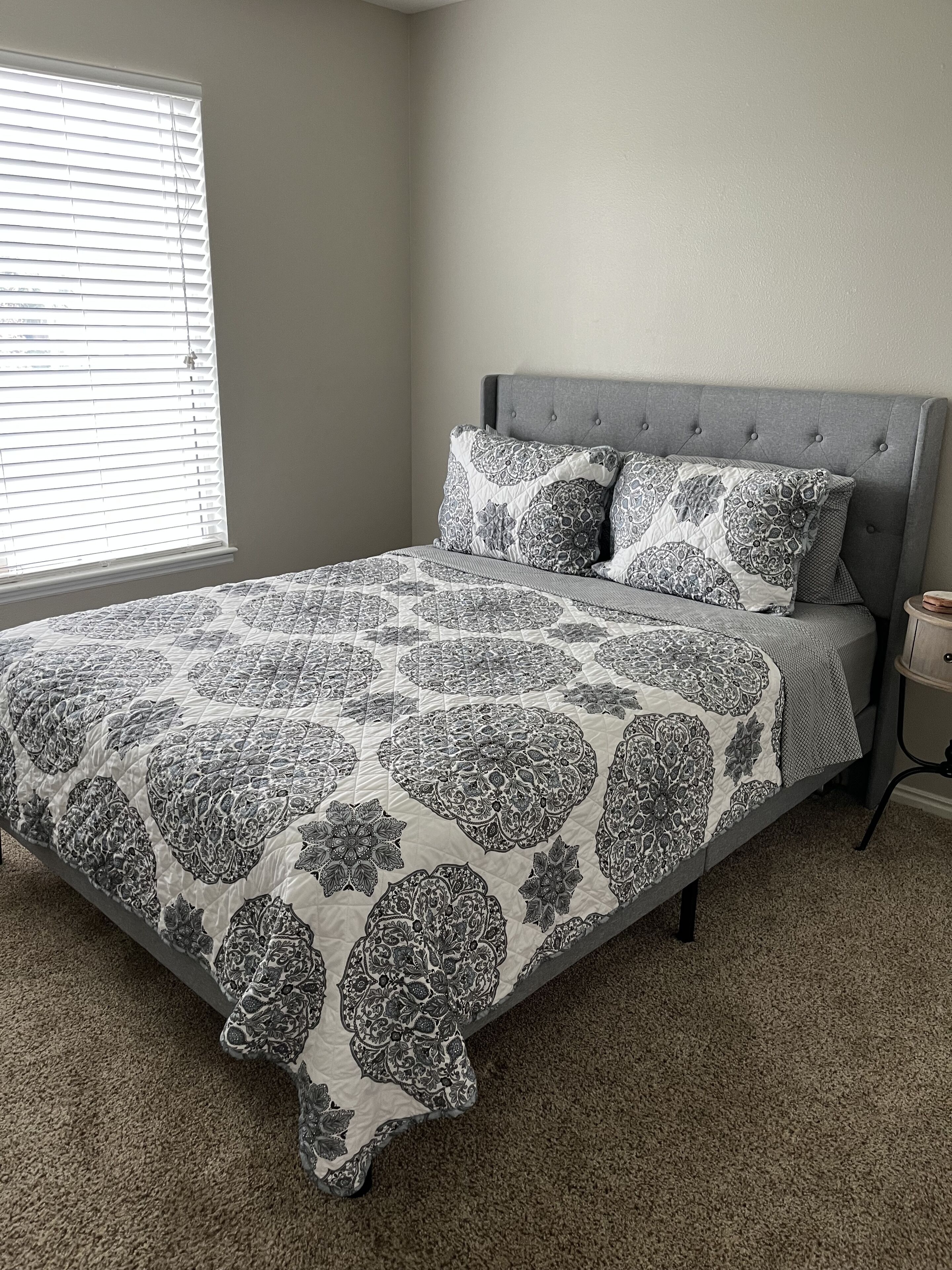 A bedroom with a large bed, grey headboard, and patterned bedding.