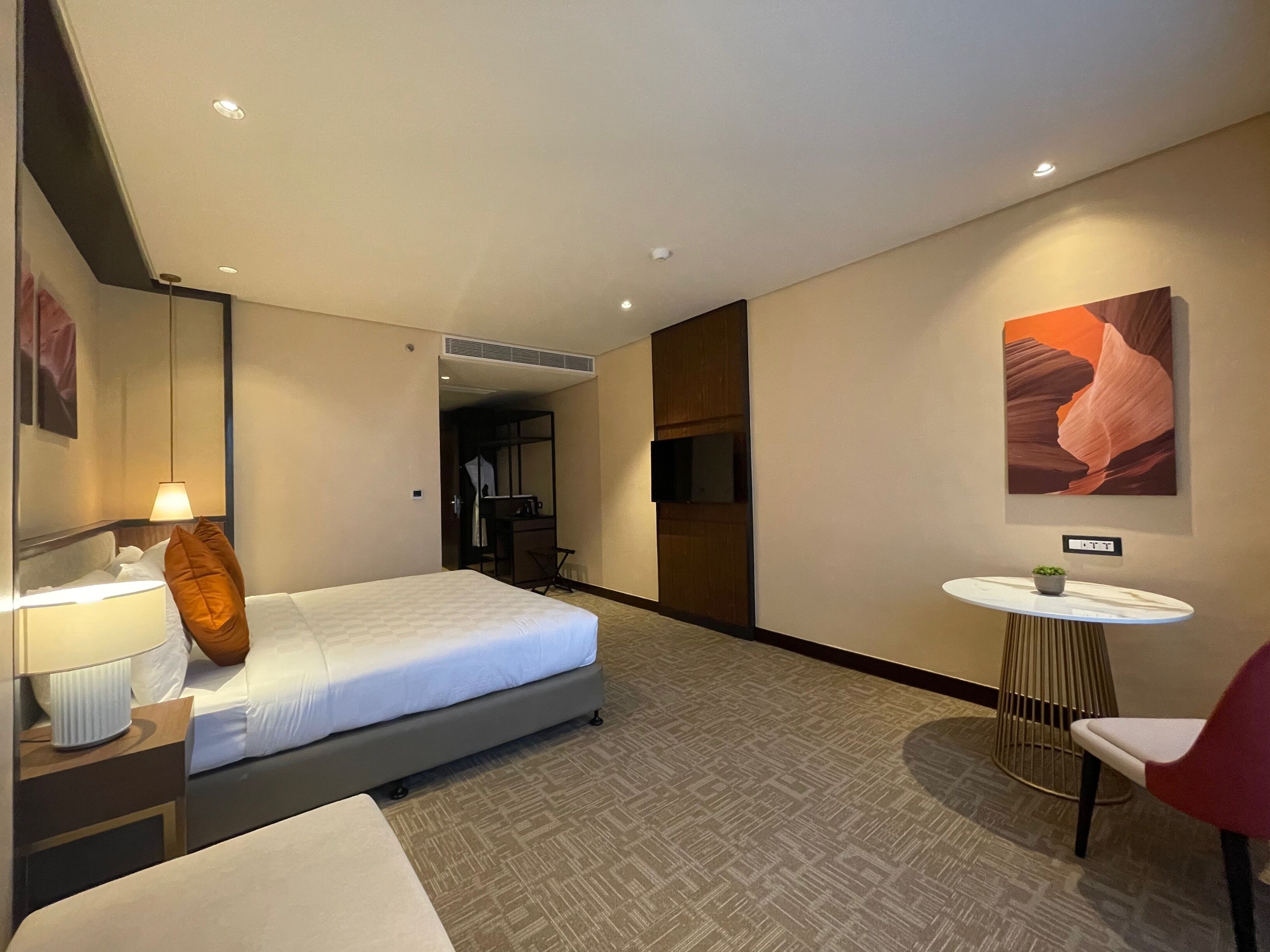 Ein Hotelzimmer mit Bett, Schreibtisch mit Stuhl, rundem Tisch mit Stuhl und einem an der Wand befestigten Fernseher.