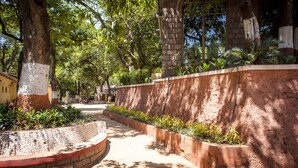 A paved pathway flanked by brick walls and greenery, leading to a building with a stone facade. - Adamo The Village (Karjat)
