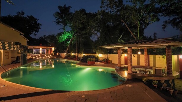 A swimming pool with a sunken seating area, surrounded by a covered patio and a small bar area. - Adamo The Village (Karjat)