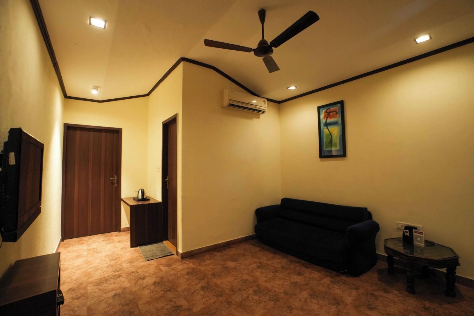 A living room with a ceiling fan, a dark-colored sofa, a small table, and an air conditioning unit on the wall.