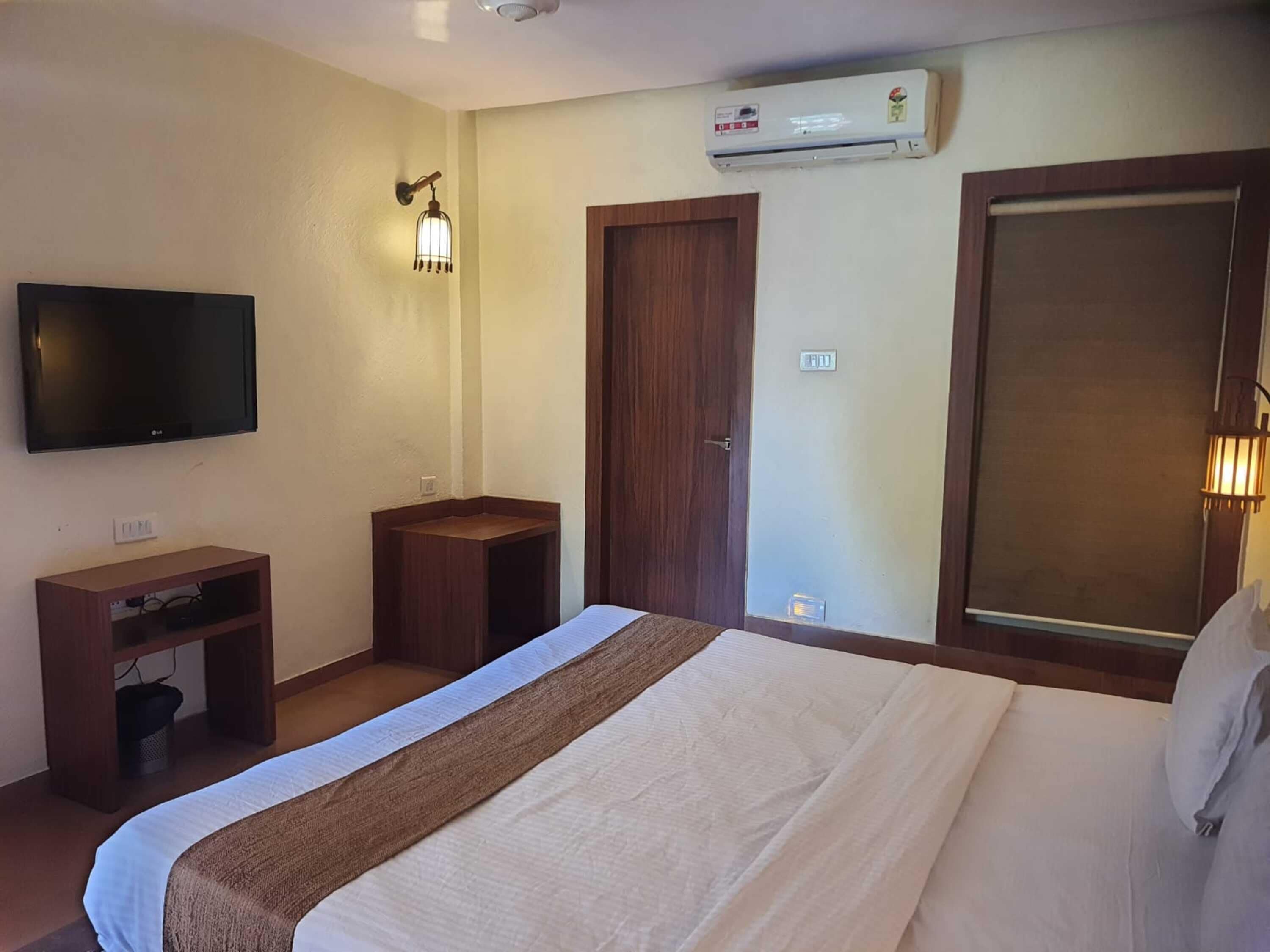 Ein Hotelzimmer mit Bett, Fernseher, Schreibtisch, Kleiderschrank und Klimaanlage.