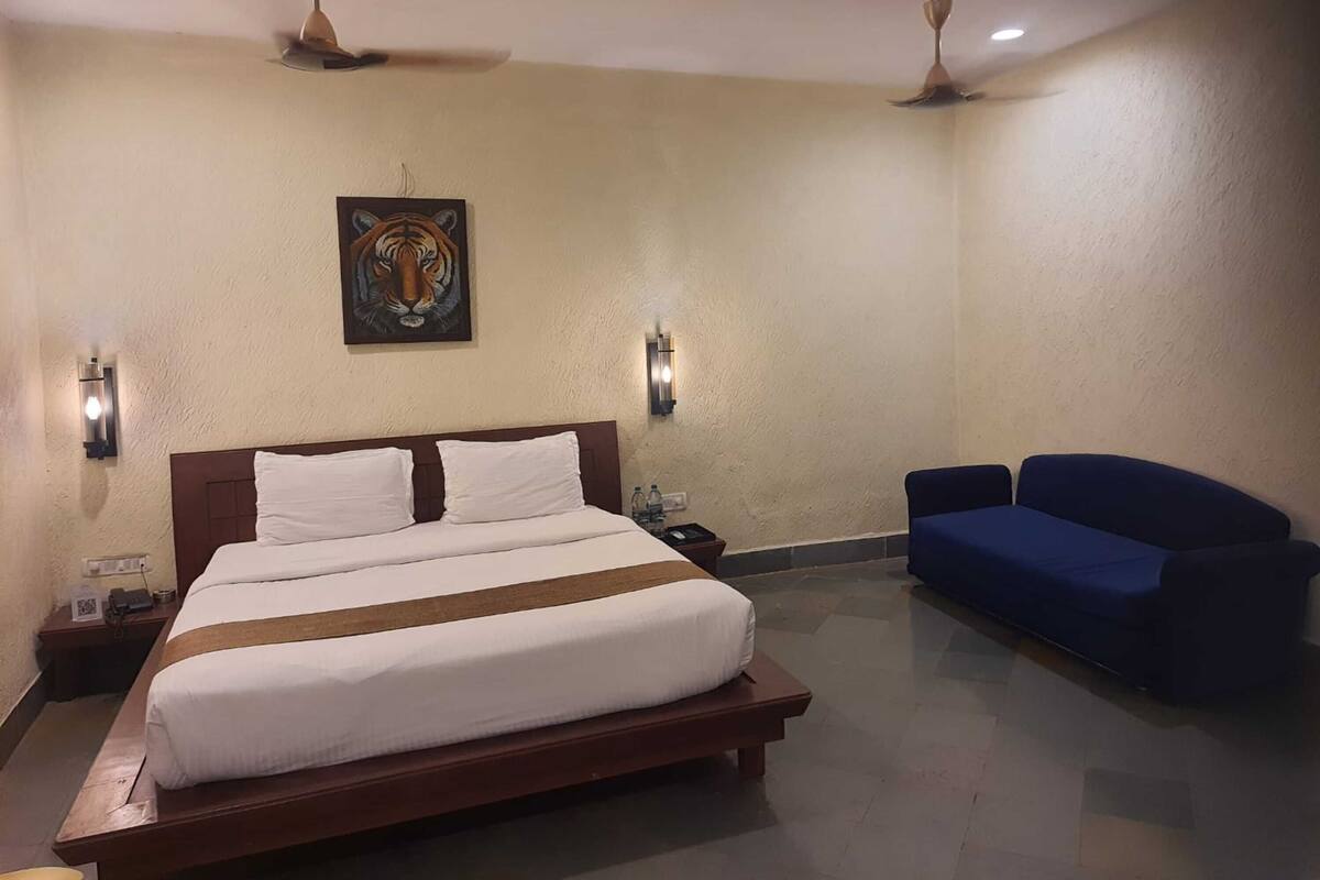 Una habitación de hotel con una cama grande, dos luces empotradas, un ventilador de techo, un cuadro de un tigre y un sofá azul.