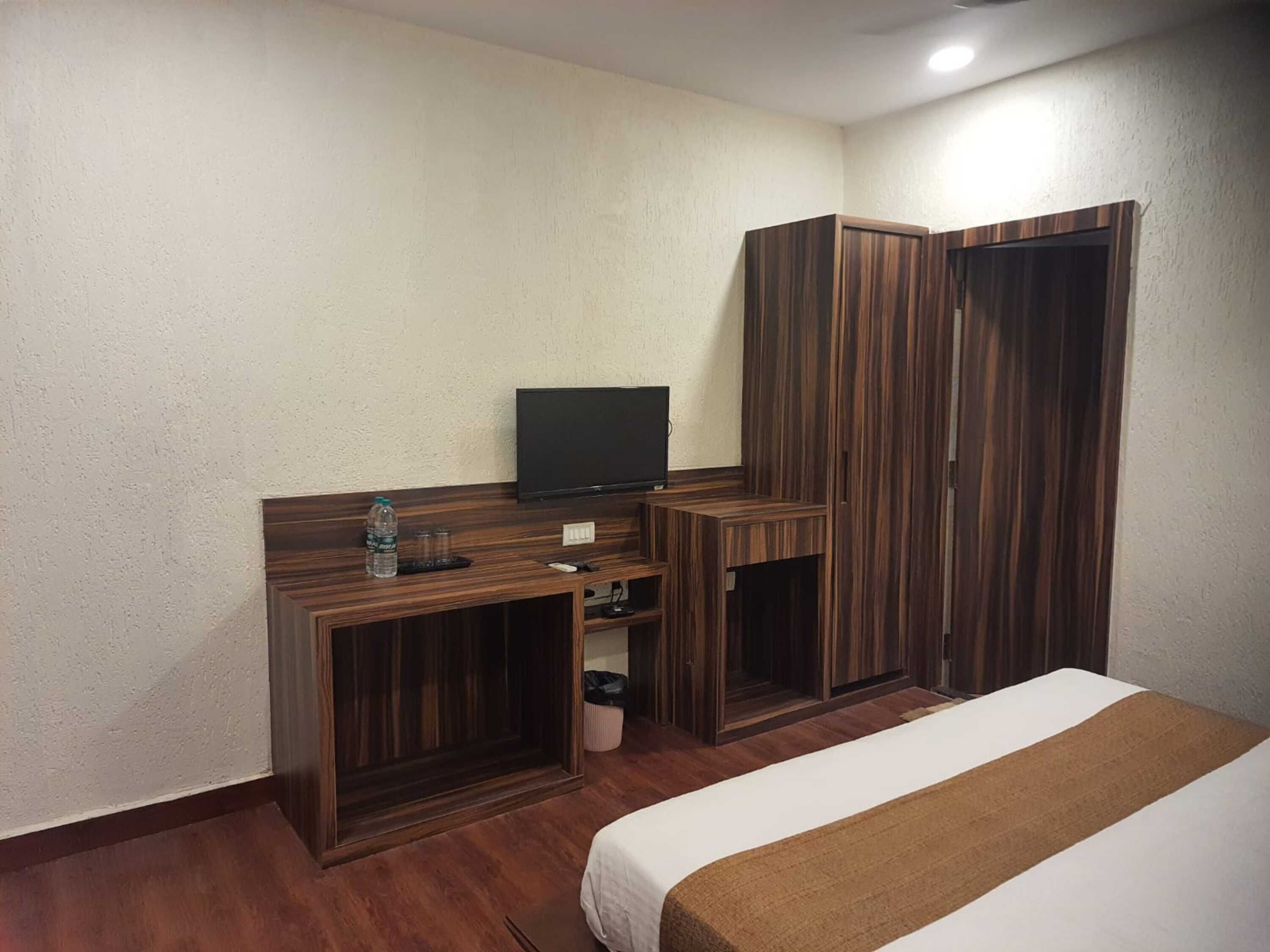 Une chambre d’hôtel avec un lit, un téléviseur posé sur un meuble en bois, une armoire et une petite poubelle.