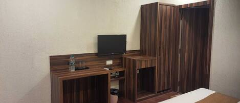 Une chambre d’hôtel avec un lit, un téléviseur posé sur un meuble en bois, une armoire et une petite poubelle.