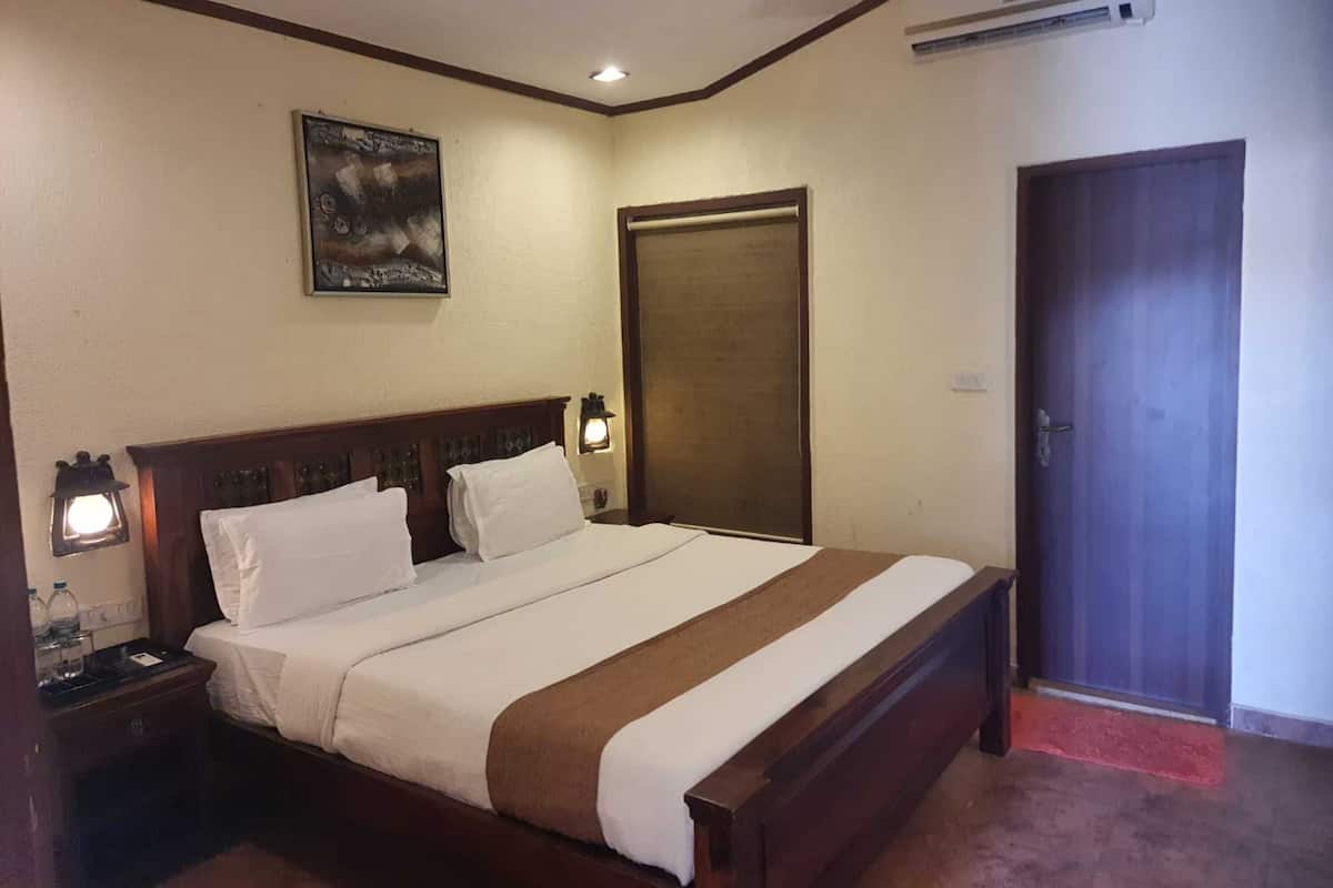 Una habitación de hotel con una cama de madera, dos lámparas de noche, un cuadro en la pared y una puerta con un felpudo rojo.