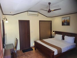 Una habitación de hotel con cama, escritorio, silla, ventilador de techo y un cuadro en la pared.