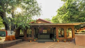 A brick building with a red roof and arched windows, surrounded by trees. - Adamo The Village (Karjat)
