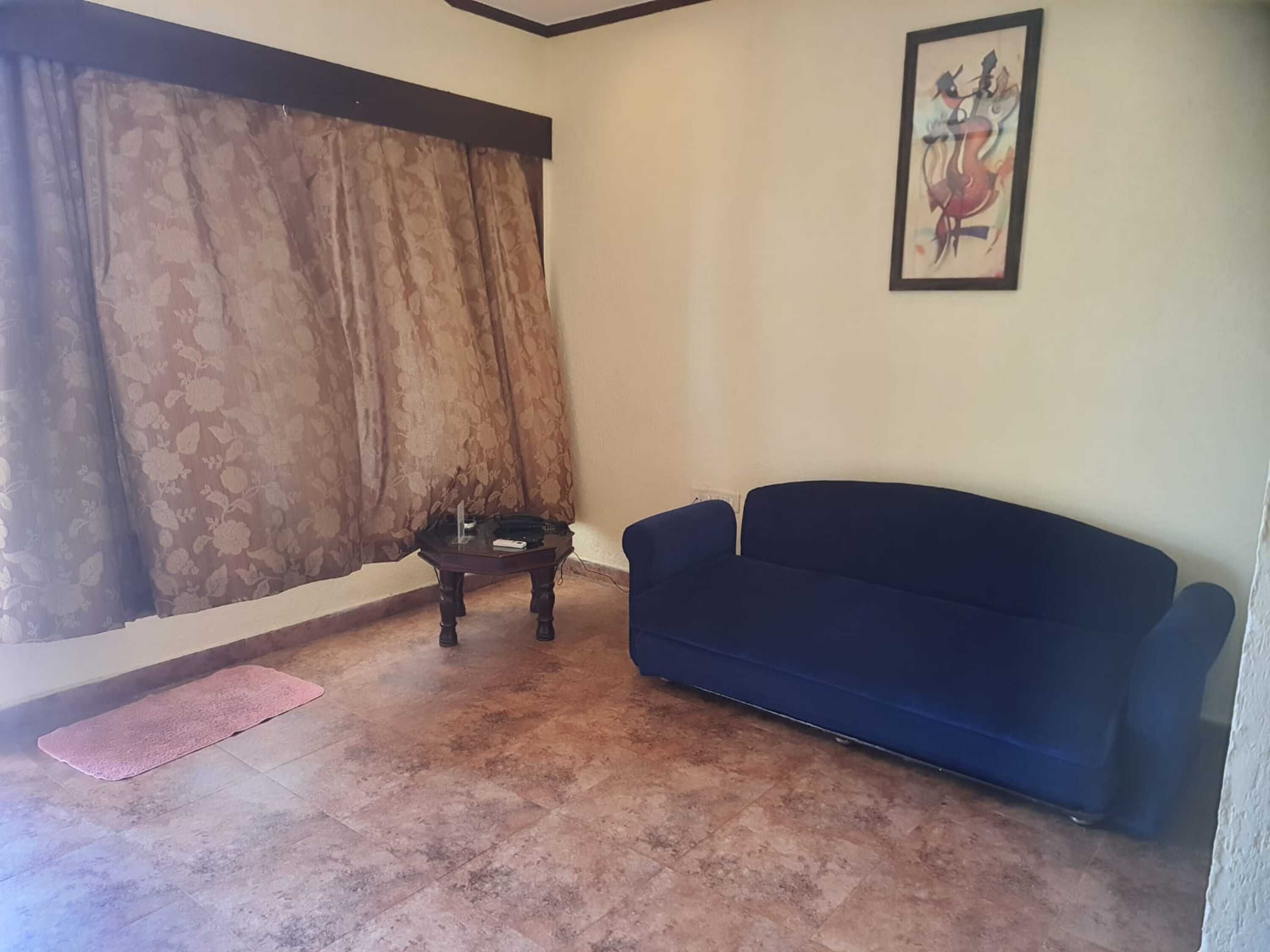 Un salon avec un canapé bleu foncé, une table basse en verre, un tapis rose et un tableau accroché au mur.