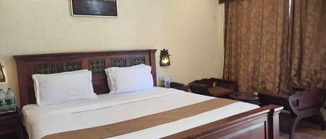 A hotel room with a large bed, a desk, a chair, a painting on the wall, and a window with curtains.