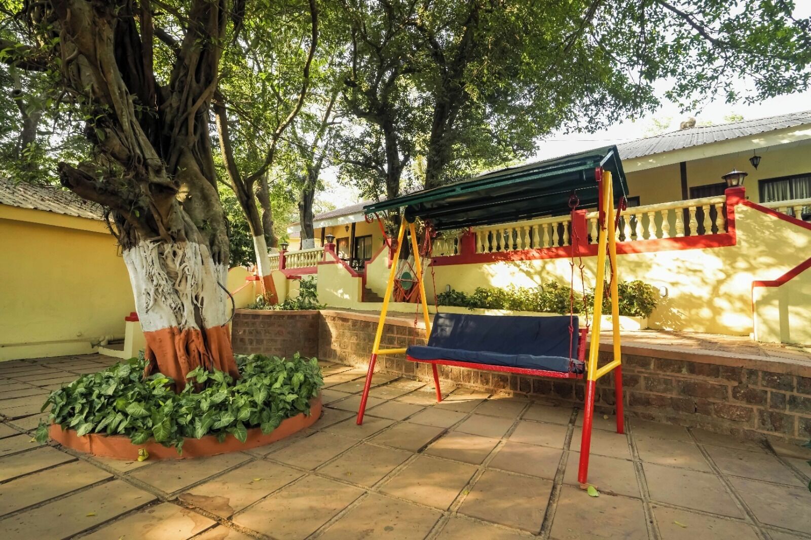 Un patio con un columpio, un árbol grande y un muro de ladrillo.