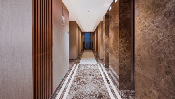 A modern hotel corridor with a marble floor, wooden paneling on one side, and a blue elevator at the end. -  Lemon Tree Hotel, Kalina BKC, Mumbai (Mumbai)