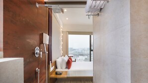A modern bathroom with a shower, a vanity, and a bed with a city view. -  Lemon Tree Hotel, Kalina BKC, Mumbai (Mumbai)