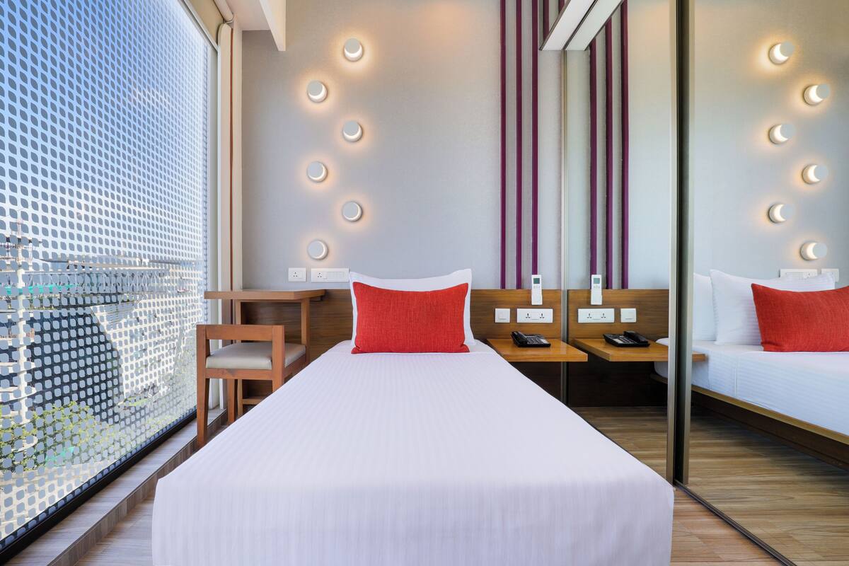 A hotel room with a large bed, bedside tables, a chair, and a view through a patterned window.