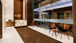A reception area with a wooden panel wall, a reception desk, and seating with a glass partition. -  Lemon Tree Hotel, Kalina BKC, Mumbai (Mumbai)