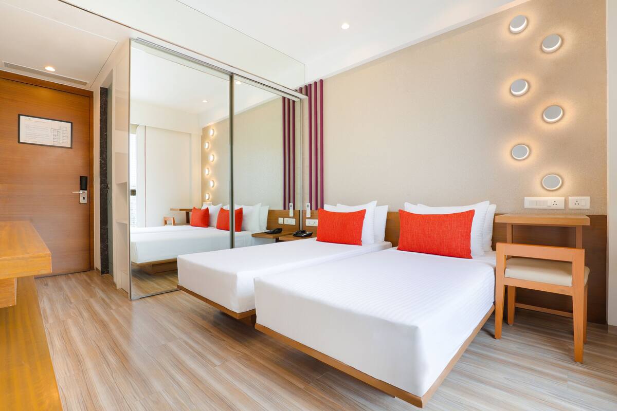 A hotel room with two beds, a mirror, a wooden desk, and a small table.