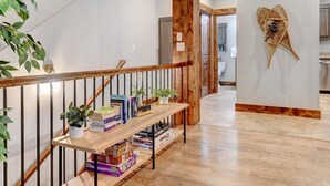 Una escalera con barandilla de madera, un estante con libros y una planta, y un adorno fijado a la pared.