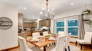 Una cocina moderna con armarios de madera, una mesa de comedor preparada para cuatro personas y un ventanal con vistas a árboles.