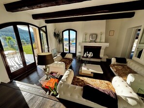 A spacious living room with a fireplace, comfortable seating, and a view of the outdoors. - Villa-Monti, Menton, Côte d'Azur (Menton)