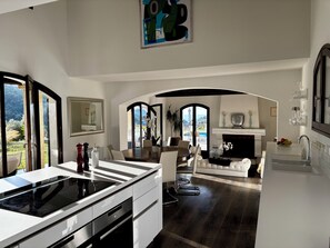 A modern kitchen with a built-in stove, white cabinetry, and a dining area with a view of the outdoors. - Villa-Monti, Menton, Côte d'Azur (Menton)