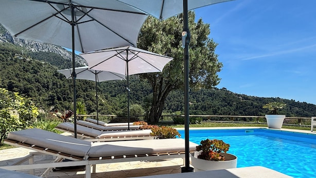 A poolside area with lounge chairs, umbrellas, and a view of a mountainous landscape. - Villa Monti: Luxury Villa, Large Pool, Air Con, Amazing Views (Menton)