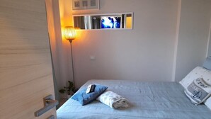 Ein ordentlich bezogenes Bett mit blauer Decke und Kissen, einer Nachttischlampe und einem an der Wand montierten Fernseher.
