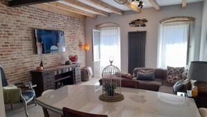 Ein Wohnzimmer mit Backsteinwand, Flachbildfernseher, Kamin, Esstisch und einer Couch mit Kissen.