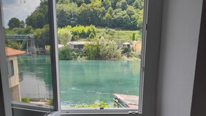 Ein Zimmer mit großem Fenster und Blick auf einen Fluss und grüne Landschaft.