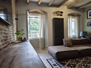 Una sala de estar acogedora con pared de ladrillo, un banco de madera, un sofá con un cojín de oso de peluche y una alfombra estampada.