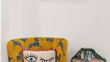 A room with a yellow armchair featuring zebra patterns, a small side table with a plant, and two framed artworks on the wall.