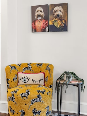 Quarto com poltrona amarela com estampas de zebra, uma mesinha de apoio com uma planta e duas obras de arte emolduradas na parede.