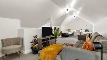 Een moderne loft slaapkamer met een groot bed, een grijze bank, een televisie en een bureau.