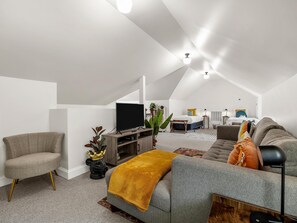 Un dormitori loft modern amb un llit gran, un sofà gris, una televisió i una zona d'escriptori.