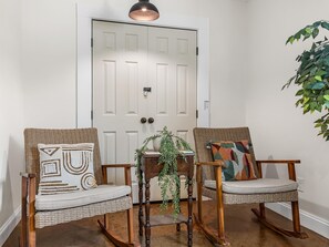 A room with two wicker rocking chairs, a small table with a plant, and a white door with a key lock. - Jungalow Retreat near Swamp Rabbit Trail! (Greenville)