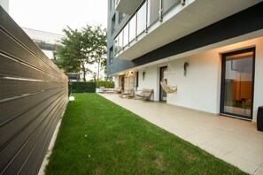 A modern building with a flat roof, a balcony with outdoor seating, and a well-maintained lawn. - Vacation Feel (Bucharest)