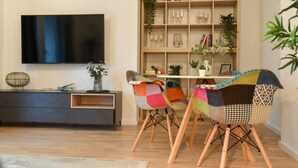 Ein modernes Wohnzimmer mit einem Flachbildfernseher, einem Holzregal und zwei bunten Sesseln.