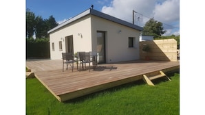 Een modern gelijkvloers huis met een plat dak, een terras met tafel en stoelen, en een kleine tuin.