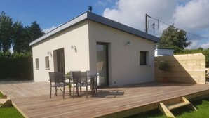 Una casa moderna de un piso con techo plano, un patio con mesa y sillas, y un pequeño jardín.