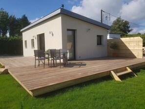 A modern single-story house with a flat roof, a patio with a table and chairs, and a small garden area.