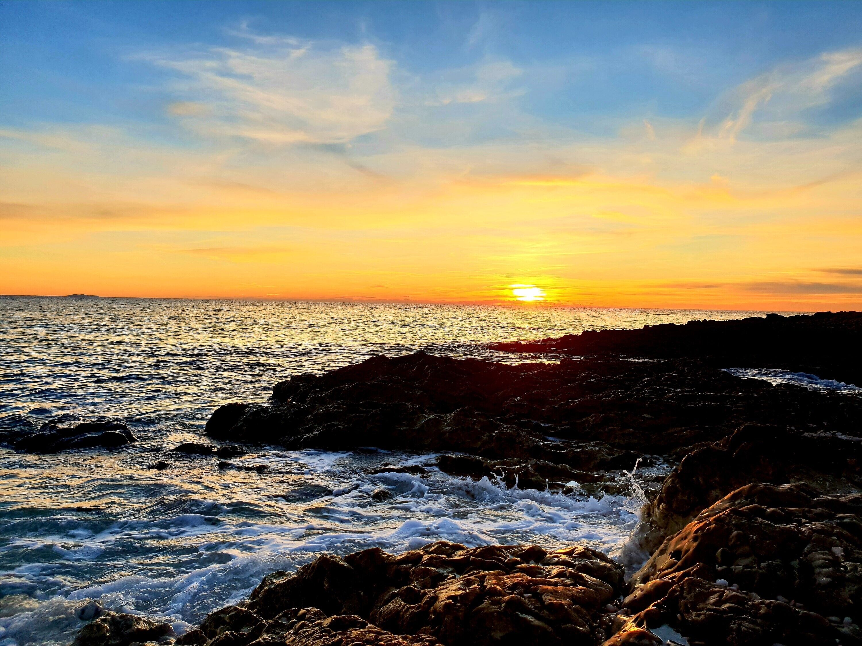 Ein Sonnenuntergang über einer felsigen Küste, Wellen schlagen an den Felsen.