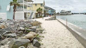 Ein Strandgrundstück mit sandigem Weg, einer Palme und einem Gebäude mit Balkon.