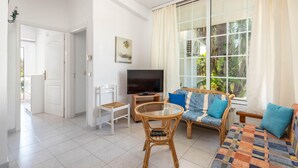 Un salon avec un canapé, des fauteuils, un téléviseur et une grande fenêtre avec des rideaux.