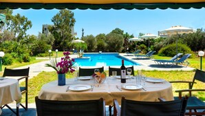 Un espace extérieur aménagé pour les repas, avec vue sur la piscine, des tables dressées et des chaises longues.
