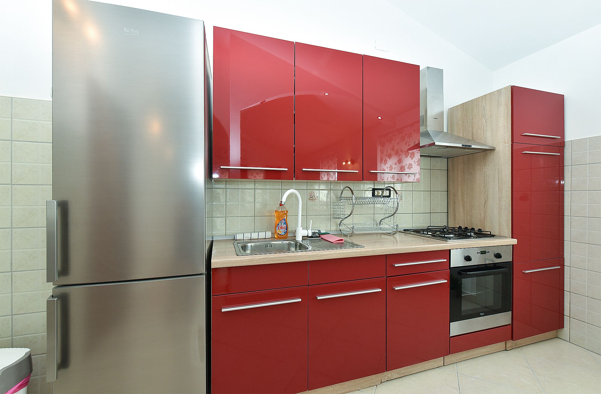 A kitchen with red cabinets, stainless steel appliances, a gas stove, and a built-in oven.