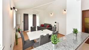 Ein modernes Wohnzimmer mit einem weißen Sofa, grauen Sesseln, einem weißen Tisch und einer Küchenzeile mit Granit Arbeitsplatten.