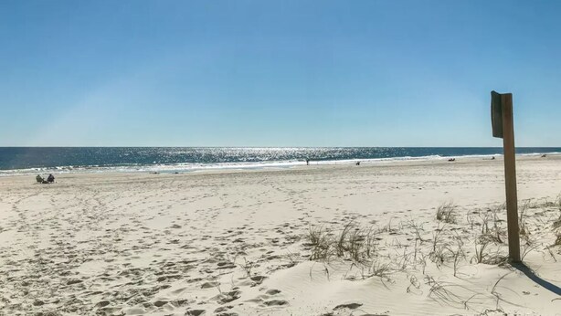 Ein sandiger Strand mit Fußabdrücken und einem hölzernen Wegweiser.