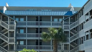 Un hotel de varios pisos con balcones, una palmera y un cielo azul despejado.