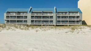 Ein Hotel am Strand mit mehreren Balkonen, einem blauen Dach und einem Sandstrand im Vordergrund.
